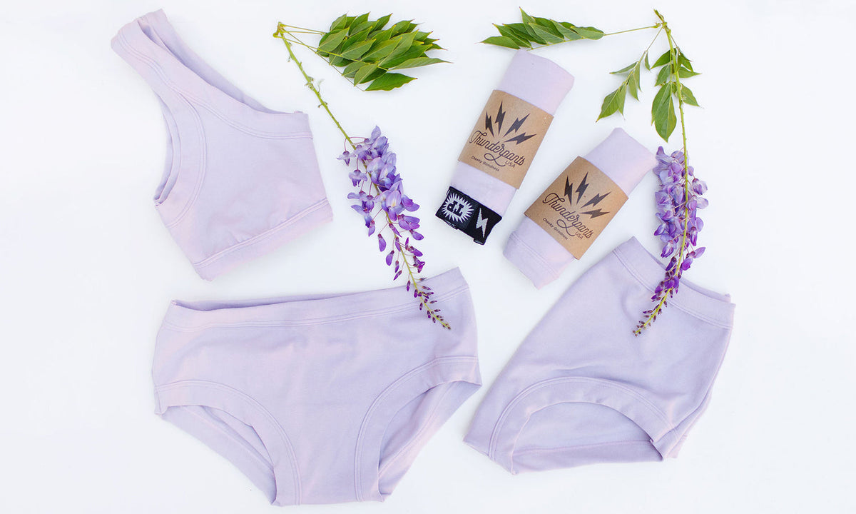 Various Thunderpants styles in a purple/grey color laying on a white background with wisteria plants.
