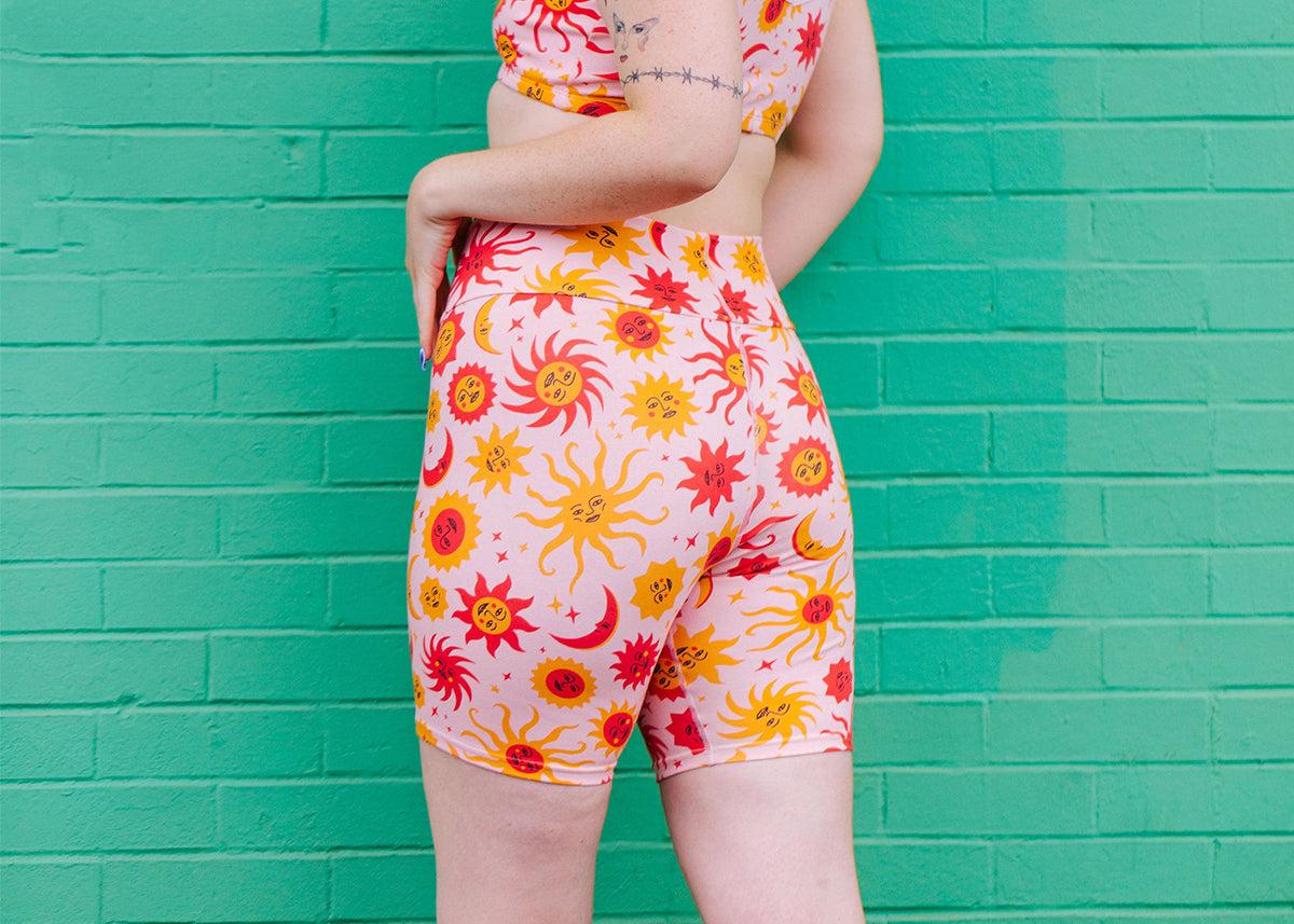 Close up of model wearing Thunderpants Bike Shorts in Luna y Sol - orange and yellow suns and moons on light pink background.
