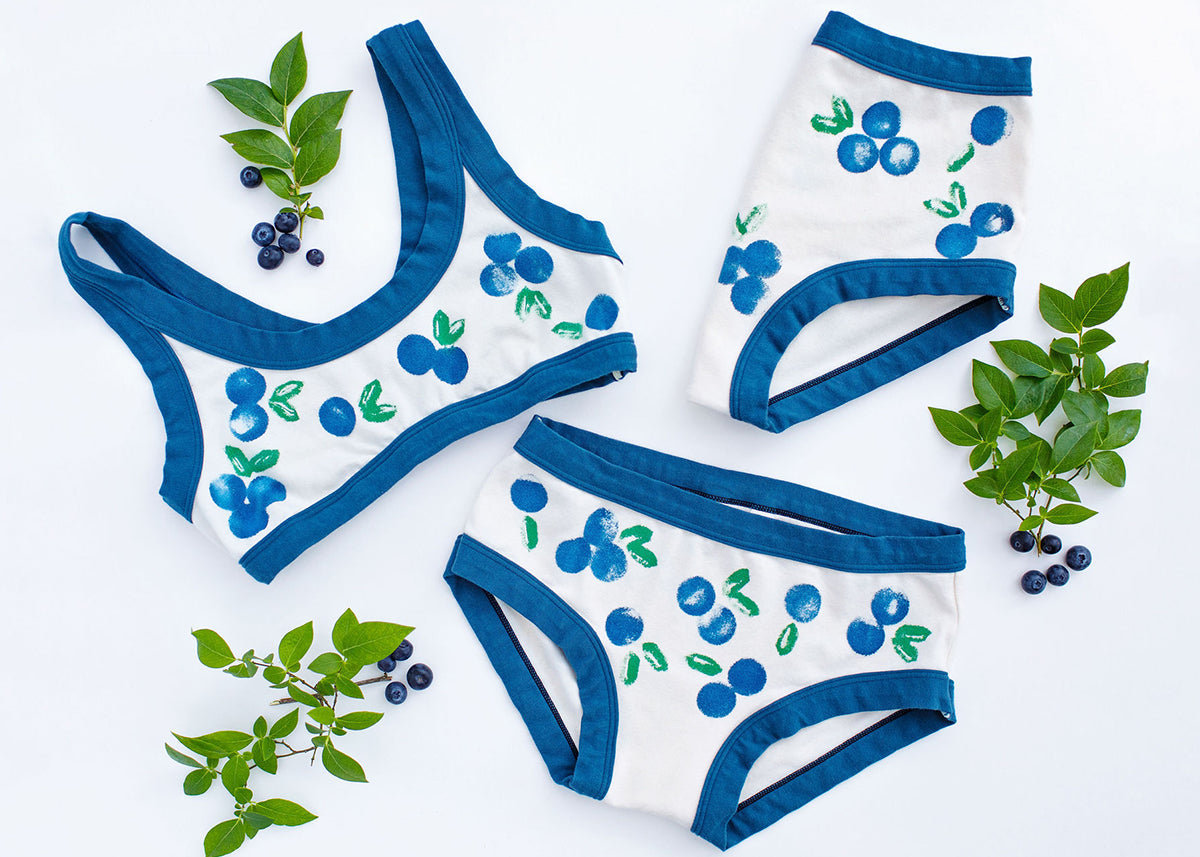 Flat lay of various Thunderpants styles in a blueberry print with blue binding.