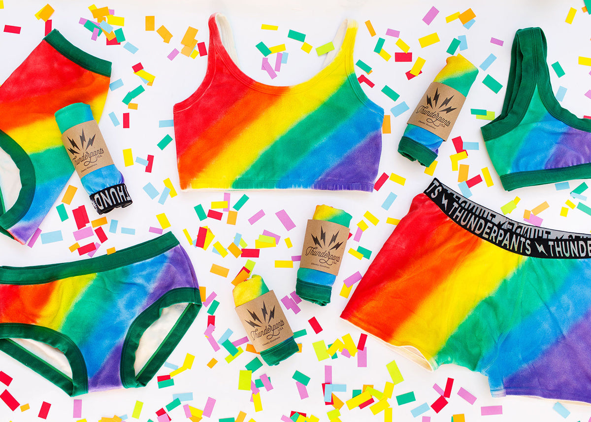 Flat lay of Thunderpants organic cotton products in many styles in the Pride Philanthropants hand painted rainbow print.