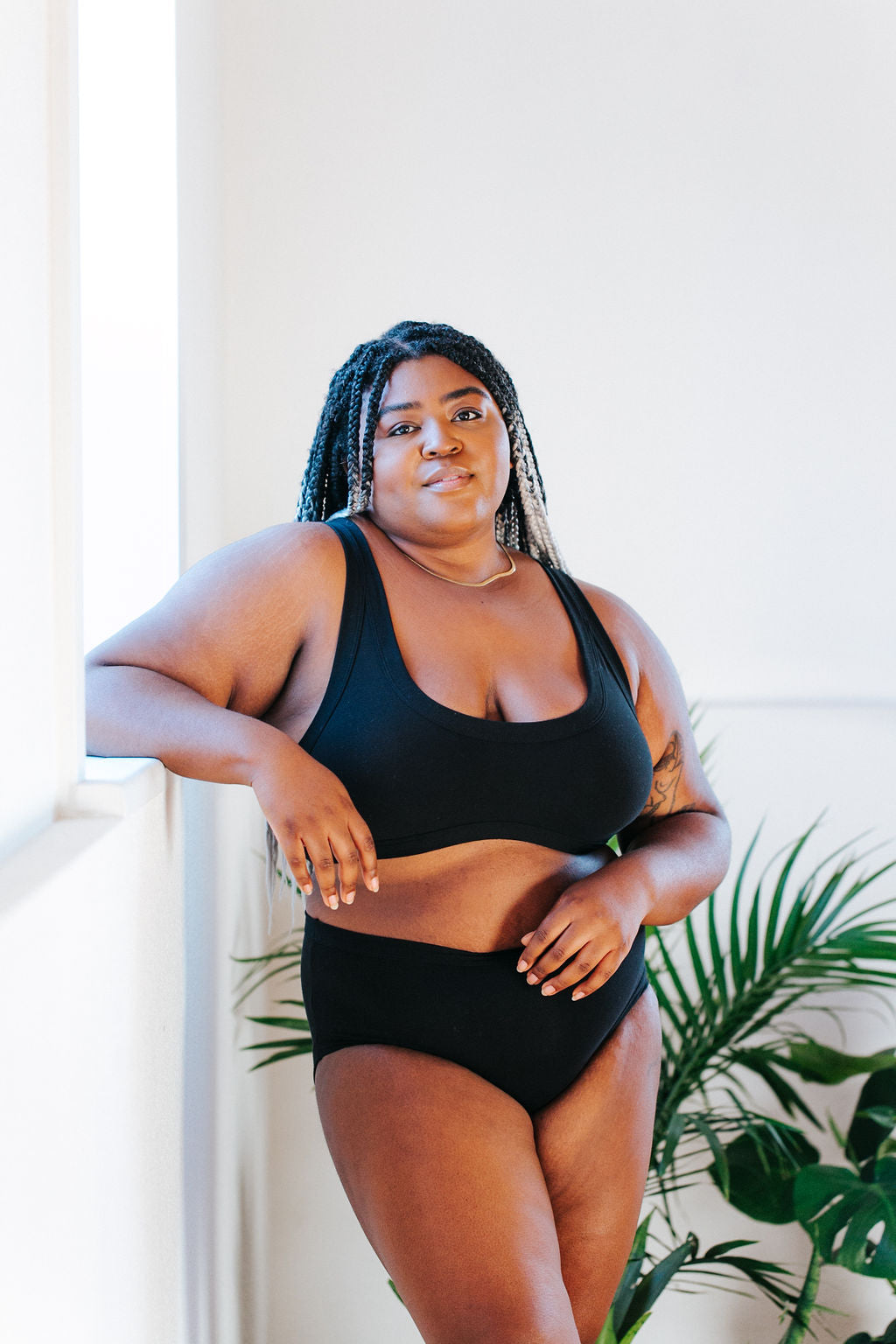 Model standing by the window wearing Thunderpants Organic Cotton Hipster style underwear and Bralette in plain Black color.