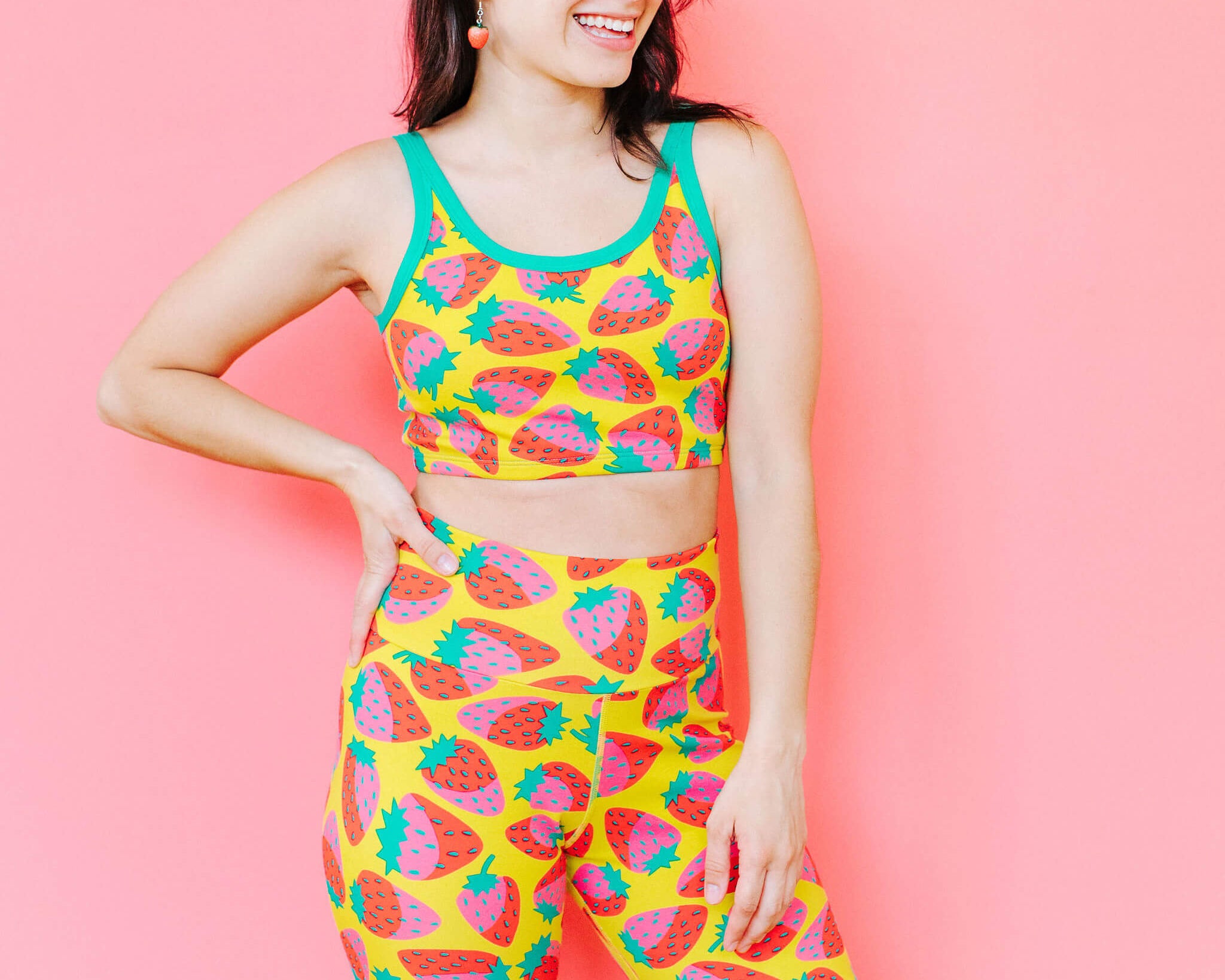 Model wearing Thunderpants Bike Shorts and Longline Bra in a Strawberry print - pink, red, and peacock green on chartreuse. 
