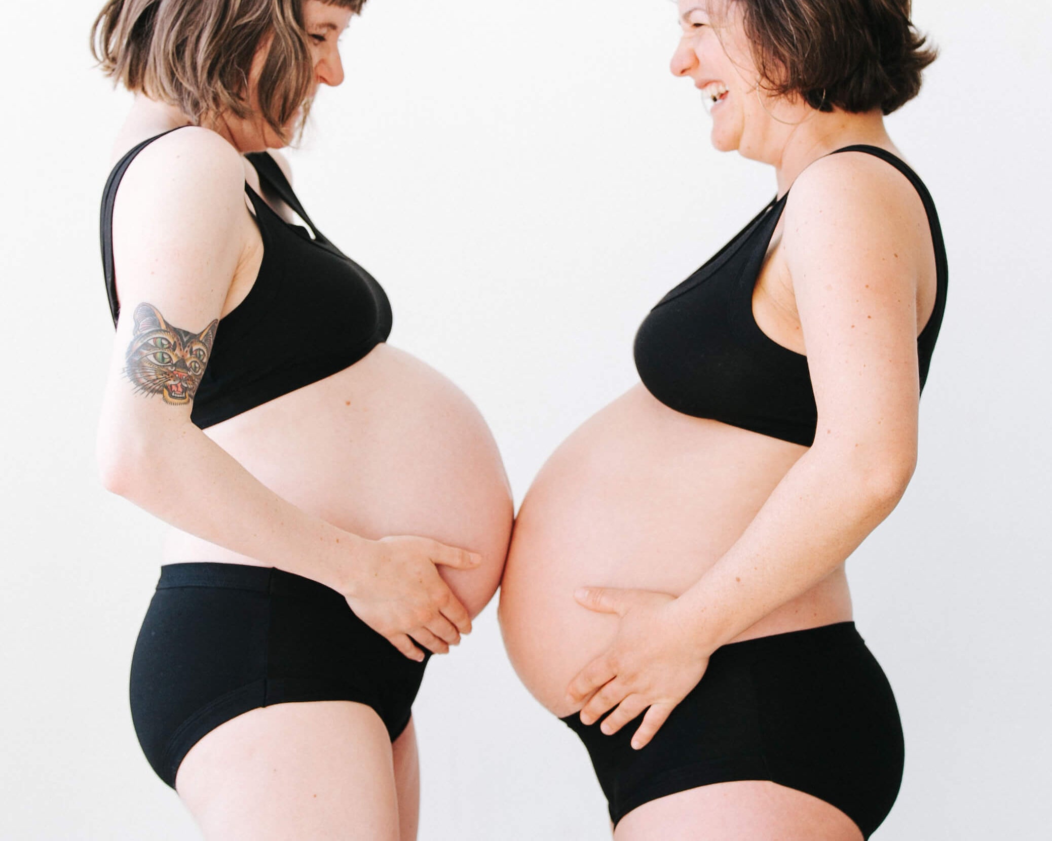 Two pregnant models wearing a set of Thunderpants Hipster style underwear and Bralette in Plain Black.