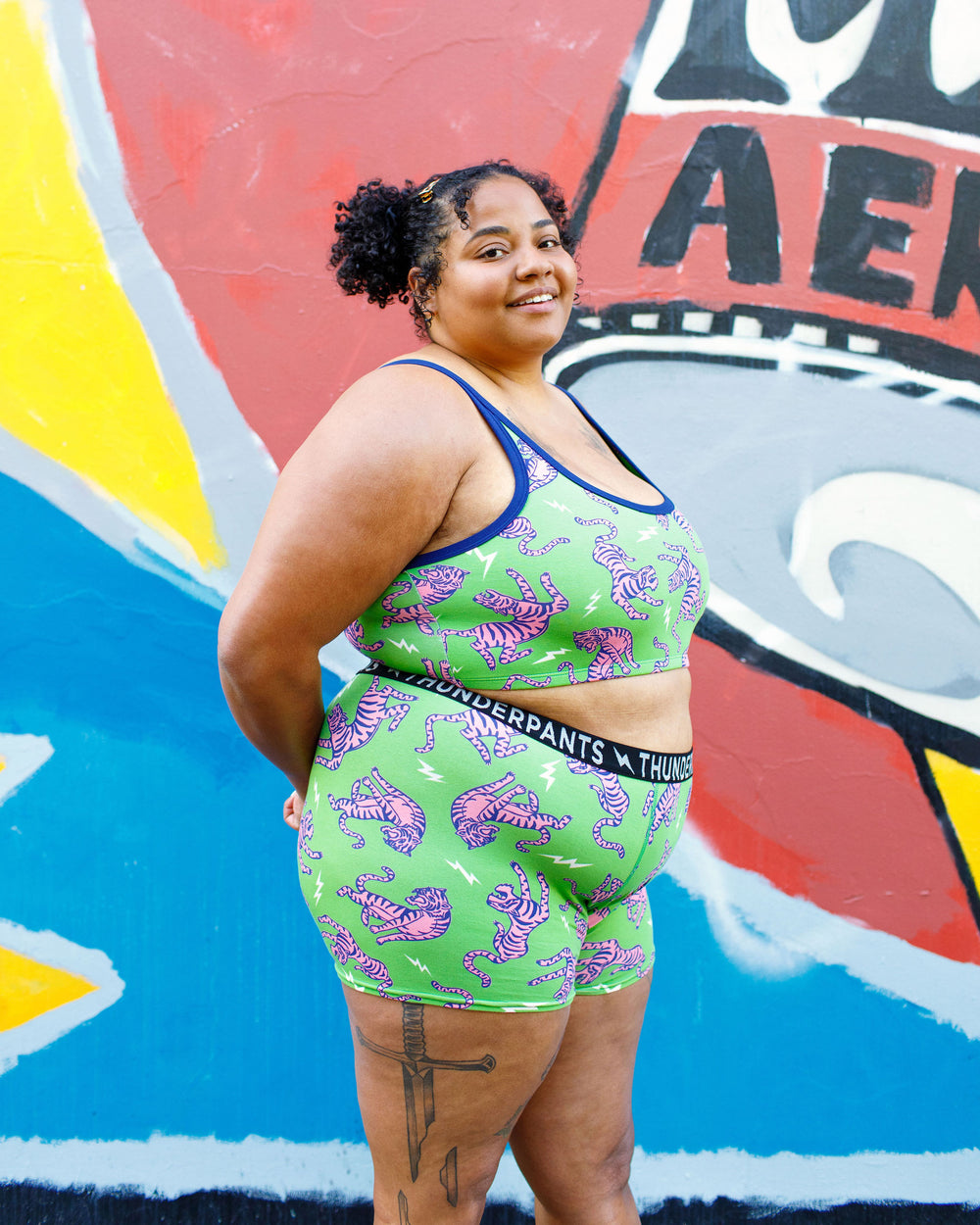 Model wearing Thunderpants organic cotton Boxer Brief and Longline Bra in Electric Tiger - green with pink and blue tigers and white lightning bolts.