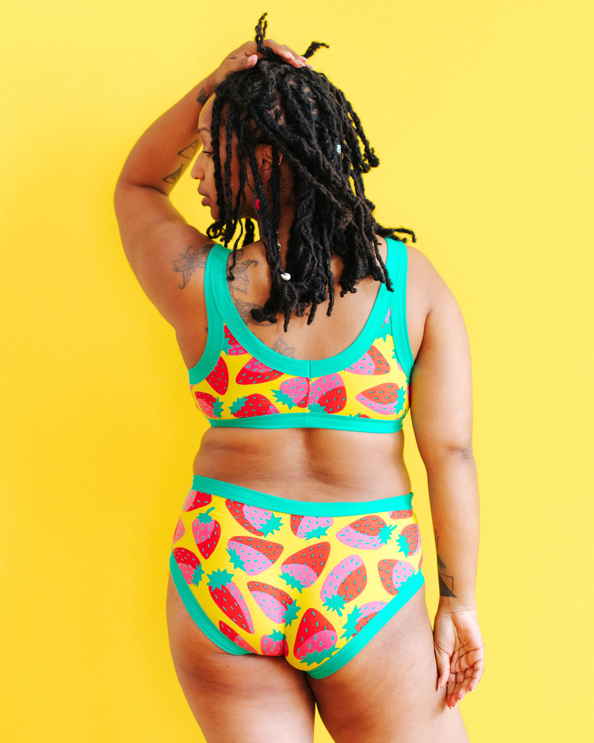 Model wearing Thunderpants Bralette and Hipster style underwear in a Strawberry print - pink, red, and peacock green on chartreuse. 