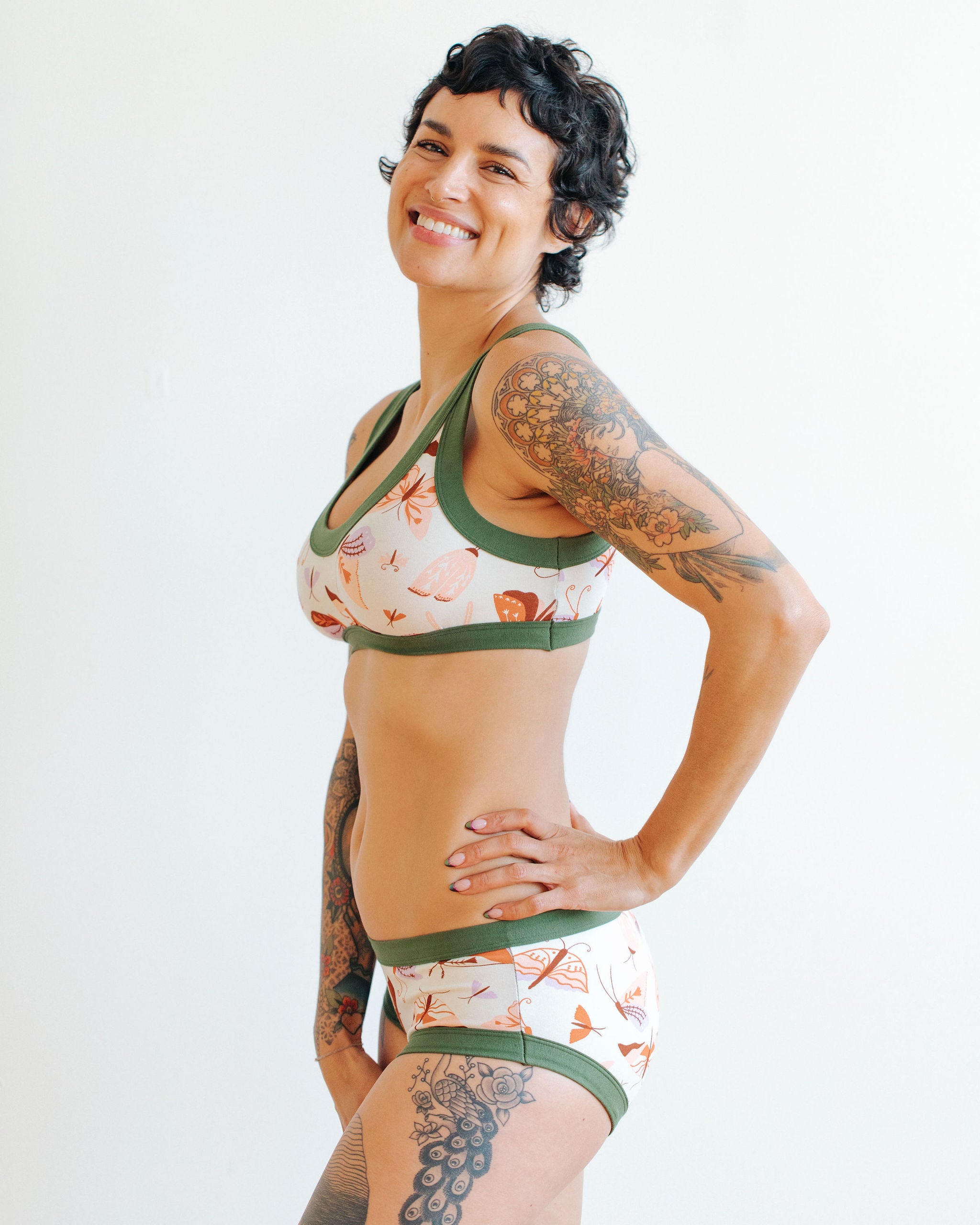 A model wearing Thunderpants Hipster style underwear and Bralette in Field Study: a moth print in red, orange, pink, and purple bound in green.