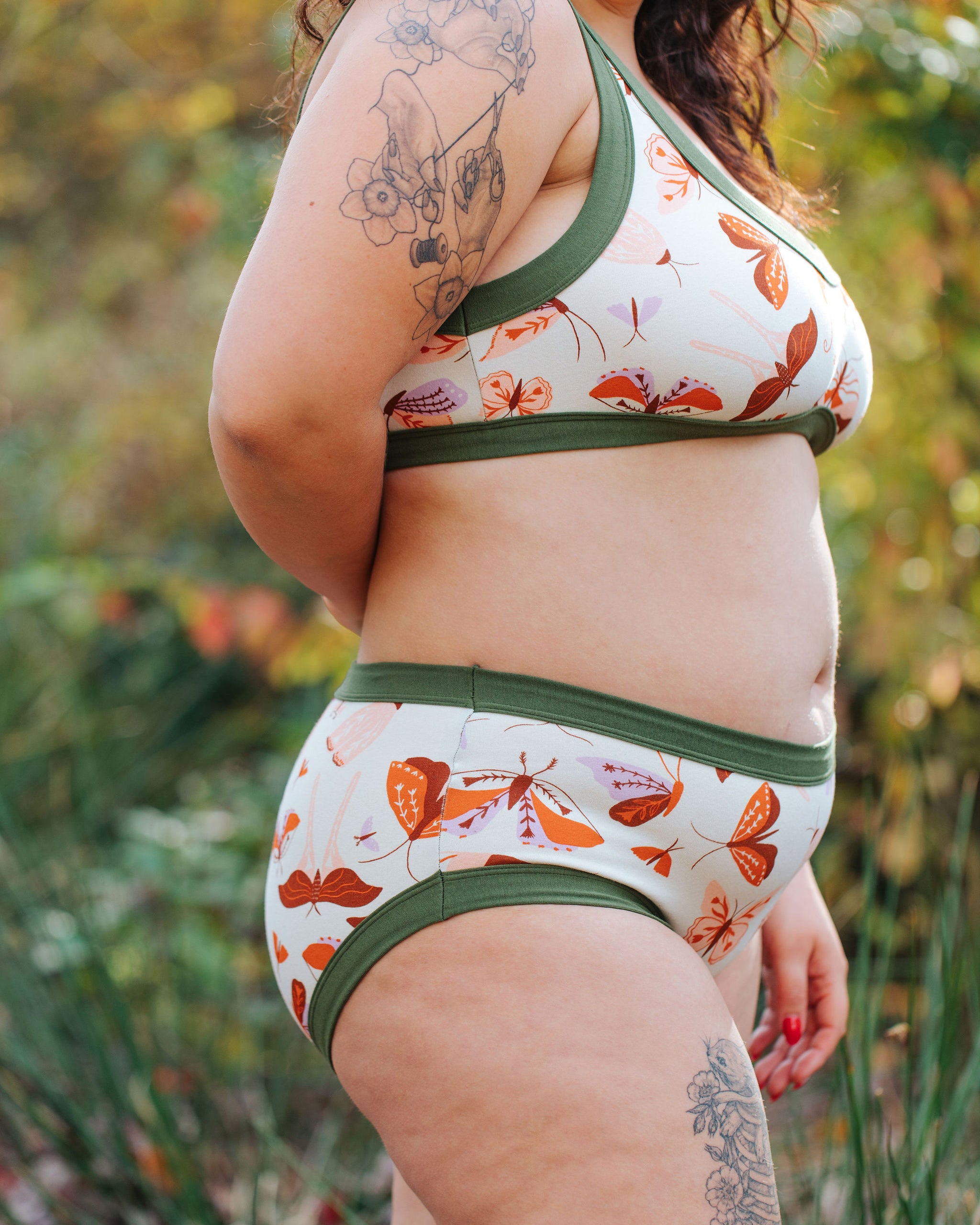 A model wearing Thunderpants Hipster style underwear and Bralette in Field Study: a moth print in red, orange, pink, and purple bound in green.
