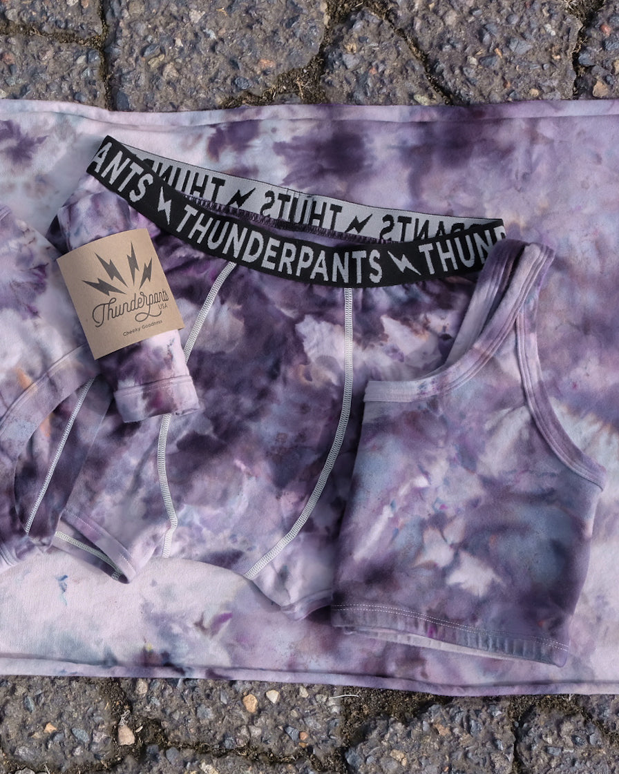 Flat lay of Thunderpants Longline Bra and Boxer Brief style underwear in Haunted Haze Ice Dye - purply grey dye pattern.