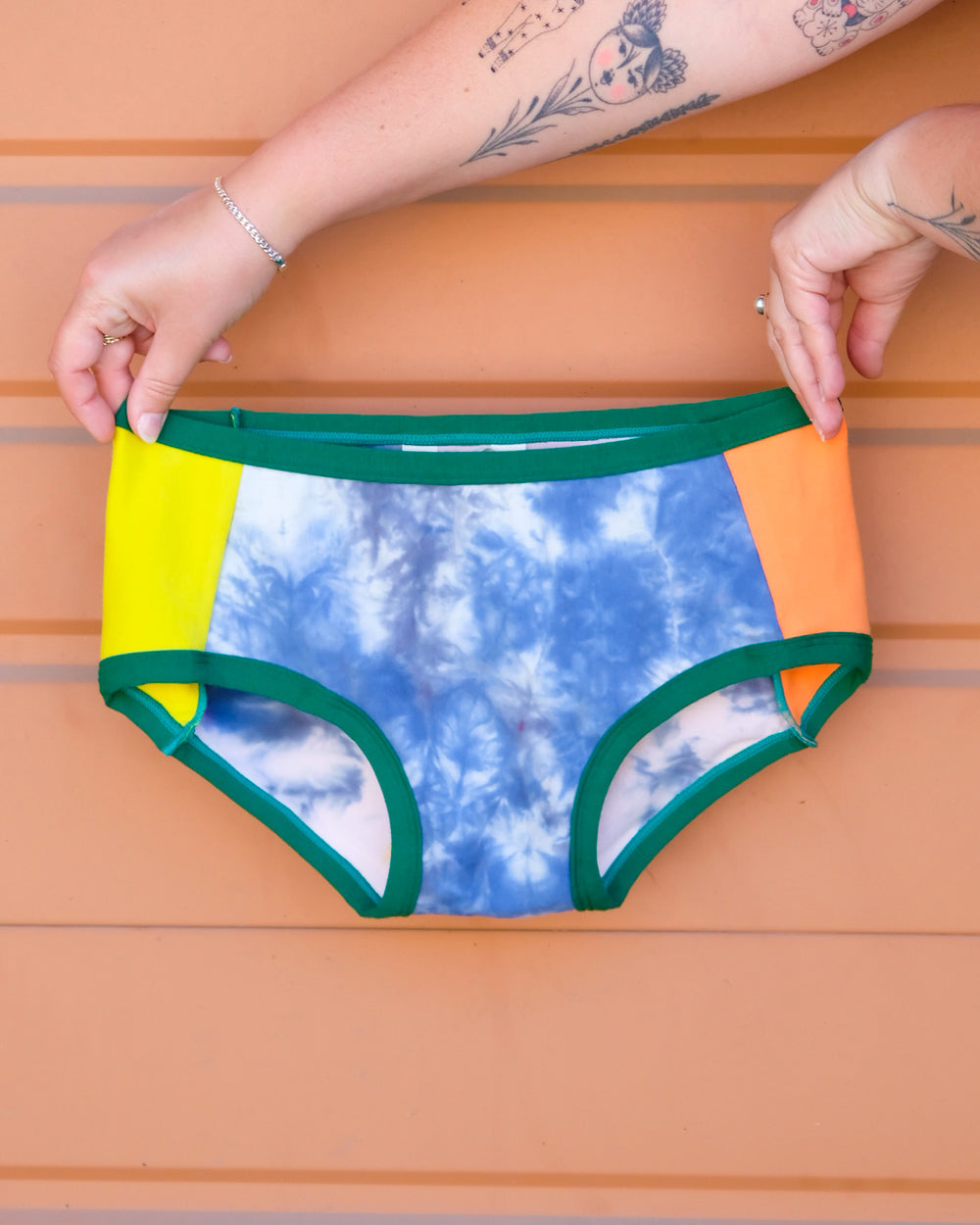 Hands holding a pair of Thunderpants Hipster style underwear in Dye Scrap Panel Pants - a mix of solids and dyed fabrics.