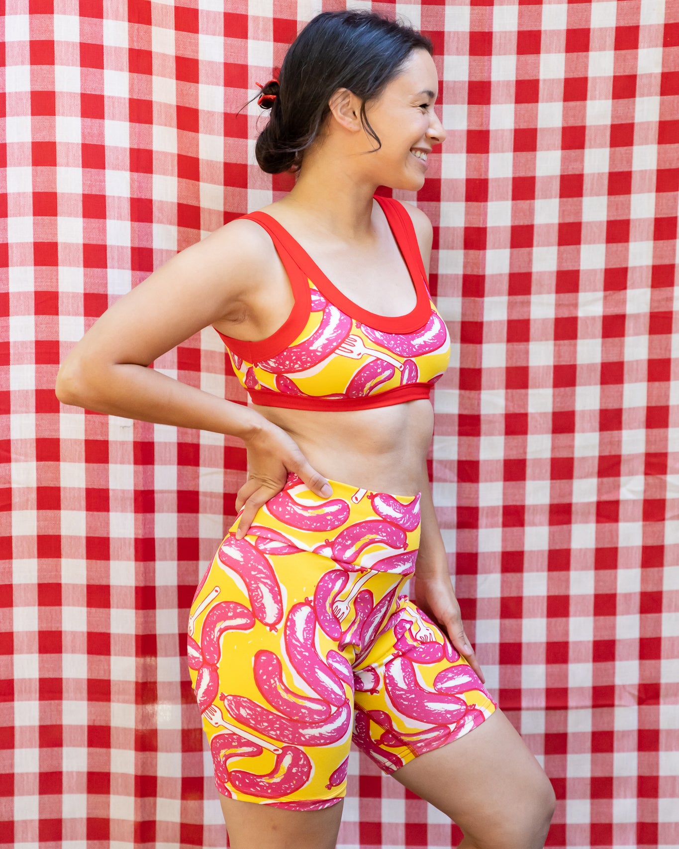 Model wearing Thunderpants Bike Shorts and Bralette in Hot Dawg! print - pink sausages on yellow background and red binding.