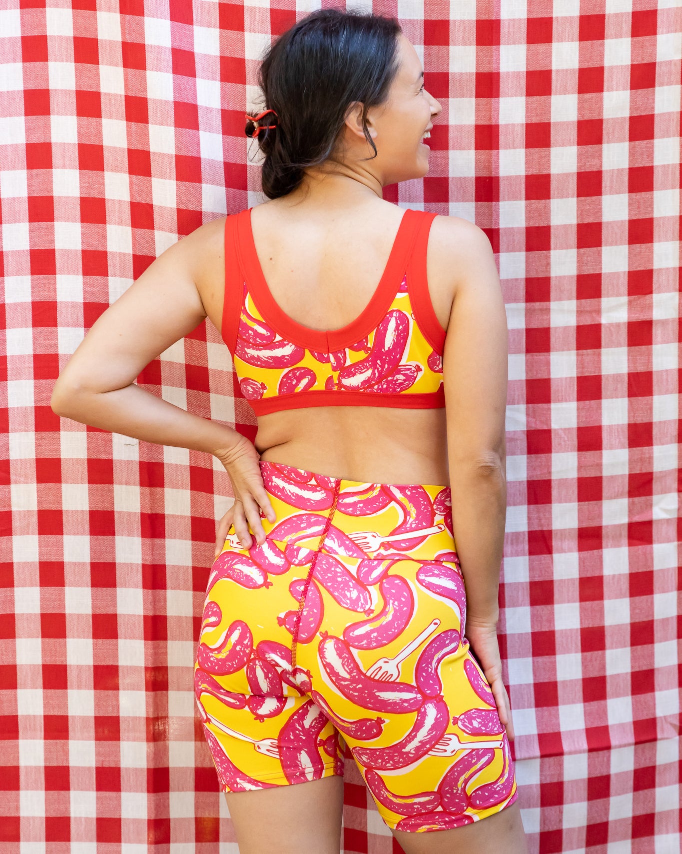 Model wearing Thunderpants Bike Shorts and Bralette in Hot Dawg! print - pink sausages on yellow background and red binding.