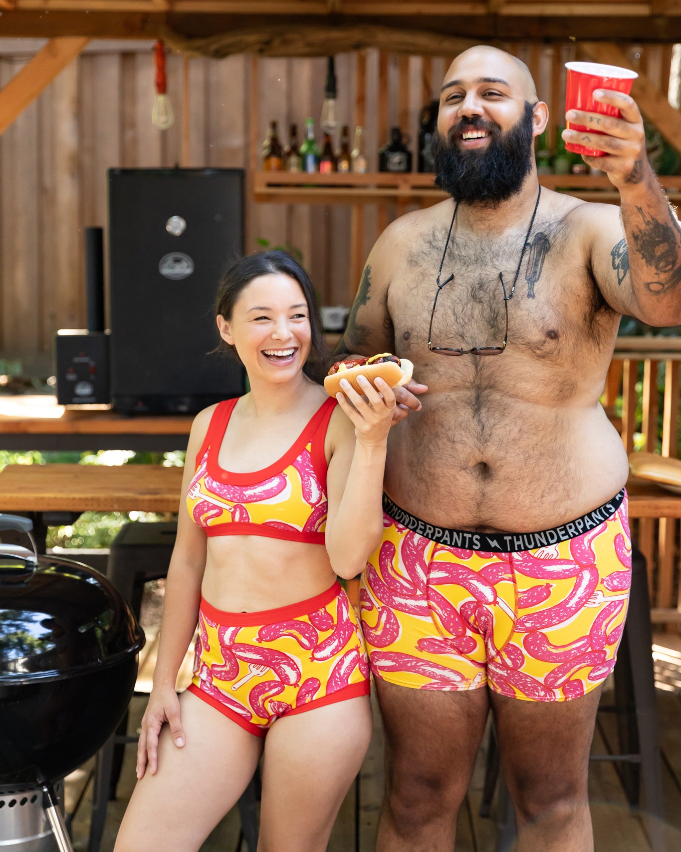 Models wearing Thunderpants Boxer Brief style underwear and other items in Hot Dawg! print - pink sausages on yellow background and red binding.