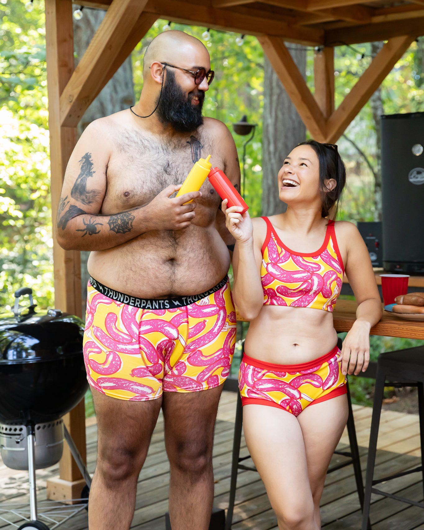 Models wearing Thunderpants Boxer Brief style underwear and other items in Hot Dawg! print - pink sausages on yellow background and red binding.