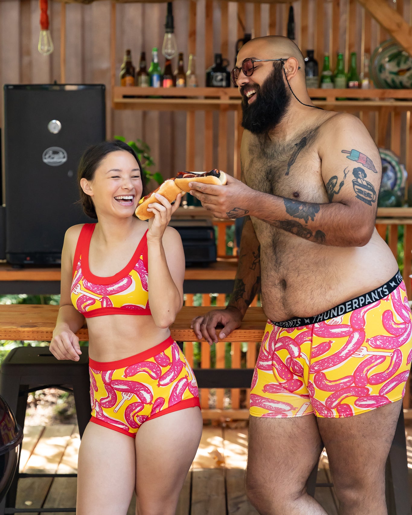 Models wearing Thunderpants Sky Rise style underwear, Bralette, and Boxer Brief in Hot Dawg! print - pink sausages on yellow background and red binding.