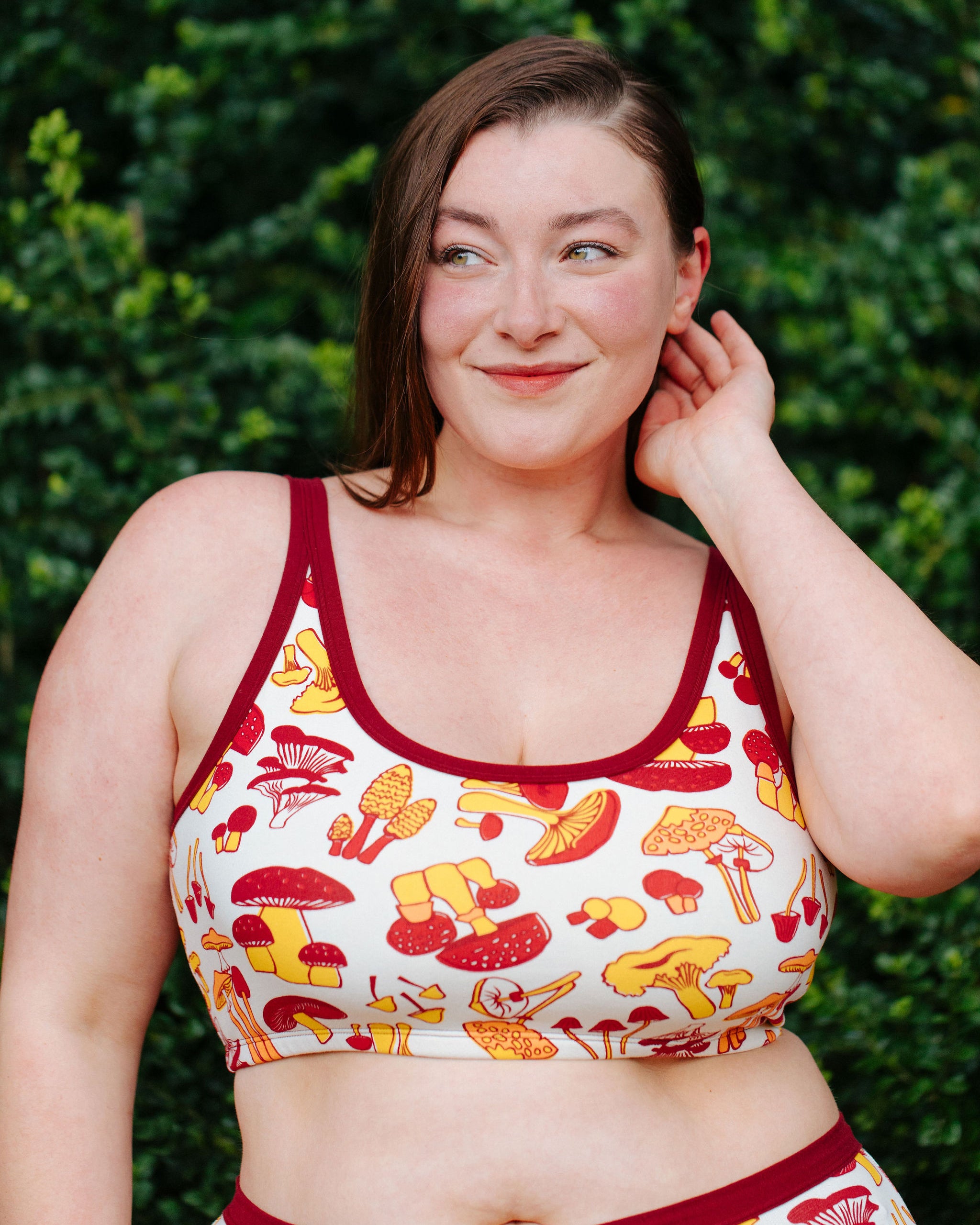 A model wearing Thunderpants Longline Bras in Whadda Fungi - red, yellow, and orange mushroom print.