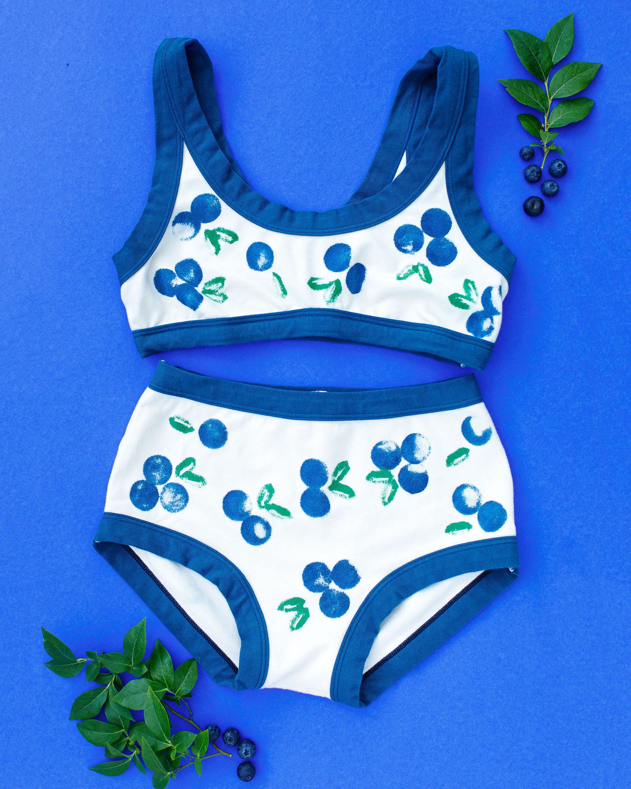 Flat lay of Thunderpants Original style underwear and Bralette with a blue and green Blueberry print and blue binding. 