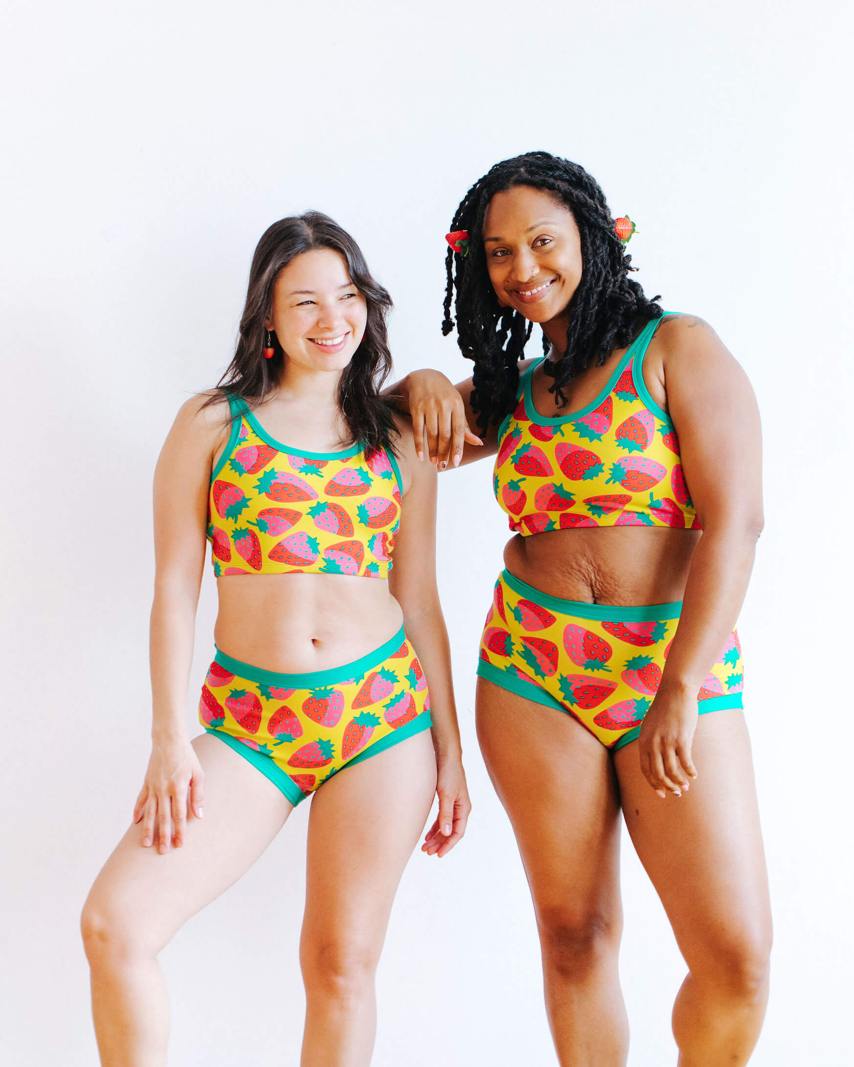 Models wearing Thunderpants Original style underwear and Longline Bra in a Strawberry print - pink, red, and peacock green on chartreuse. 