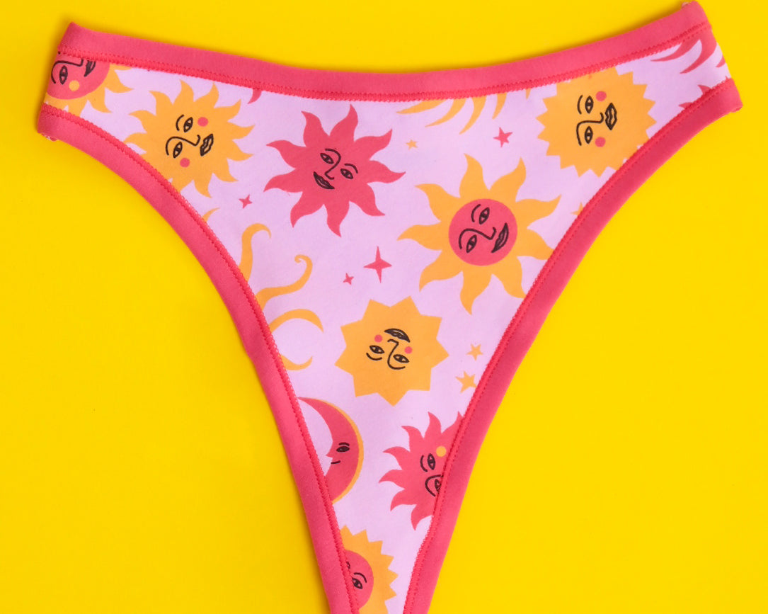 Flat lay of Thunderpants organic cotton thong style underwear in Luna y Sol print - pink and orange suns and moons.