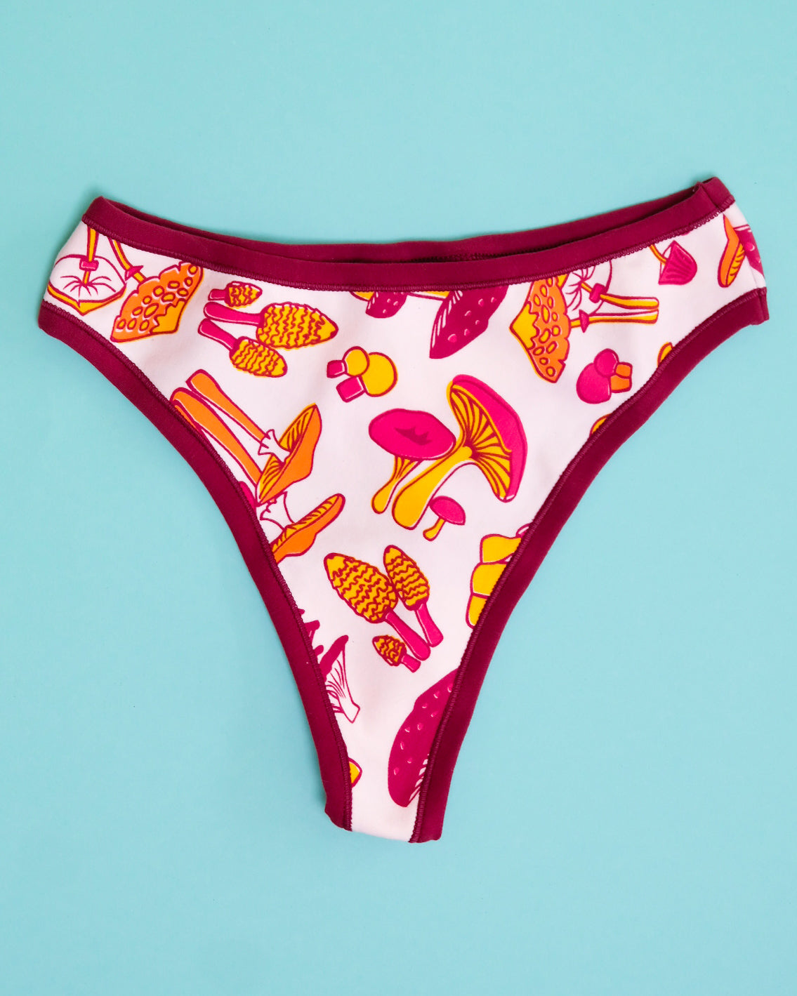 Flat lay of Thunderpants organic cotton Thong style underwear in yellow, orange, and red mushroom print.