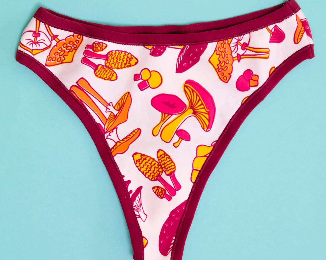 Flat lay of Thunderpants organic cotton Thong style underwear in yellow, orange, and red mushroom print.