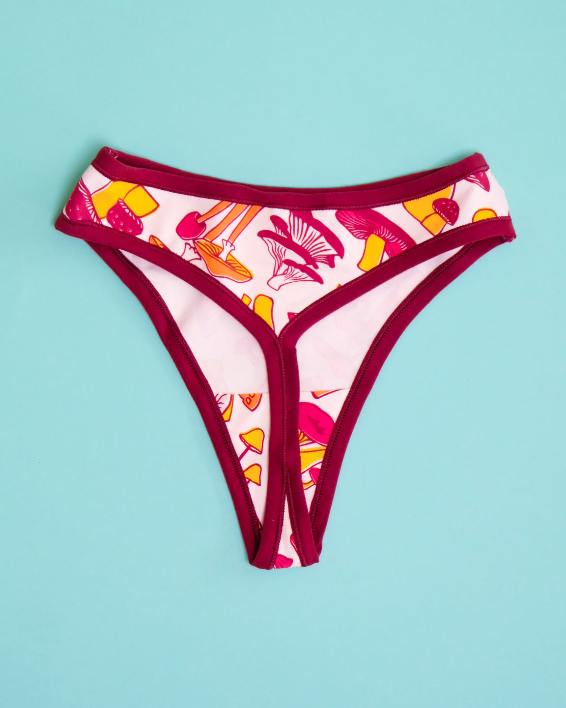 Flat lay of Thunderpants organic cotton Thong style underwear in yellow, orange, and red mushroom print.